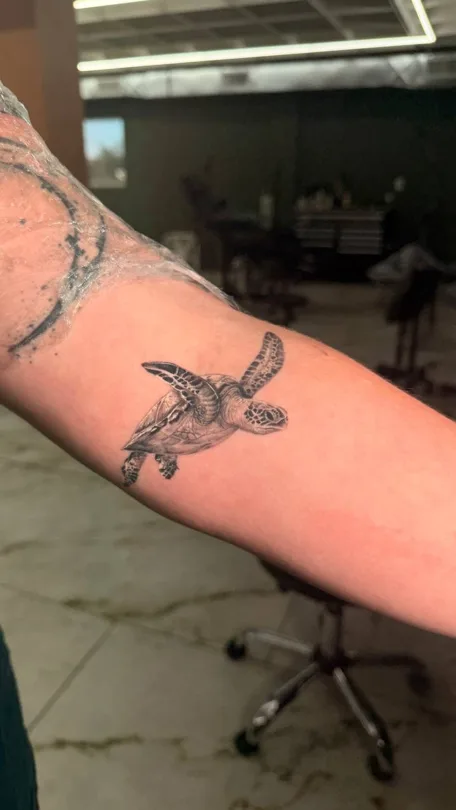 Small black and grey winged creature tattoo on an arm