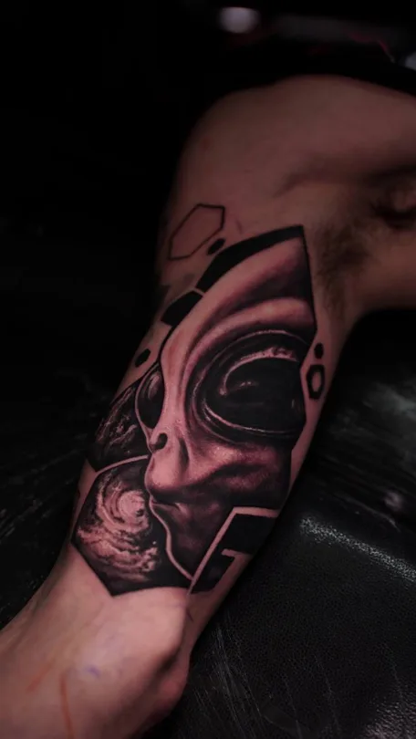 Black and grey biomechanical creature with sweeping geometric shapes tattoo on an upper arm