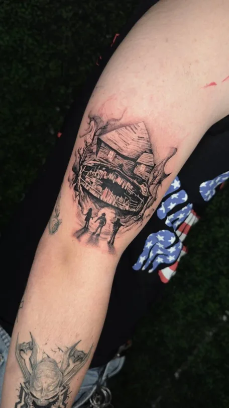 Tattoo of black and grey cabin and branches on the inner upper arm