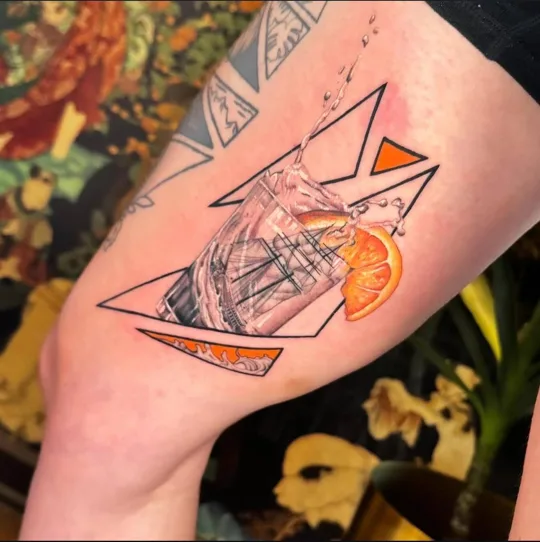 Orange slices and botanical detail within angular geometric shapes tattoo on a thigh