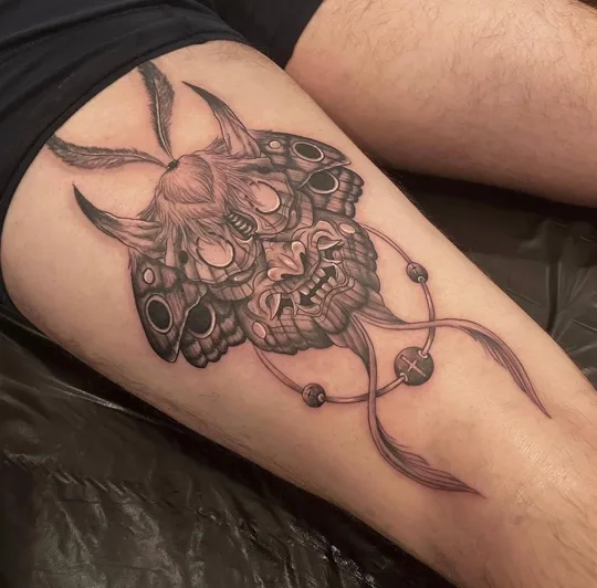 Detailed skull with curling horn-like shapes and dangling ornaments tattoo on a thigh