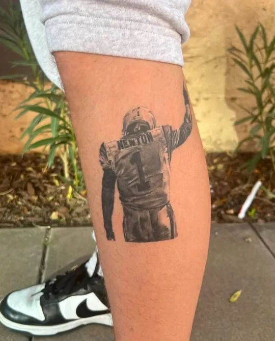 Black and grey figure with outstretched arms tattoo on a calf