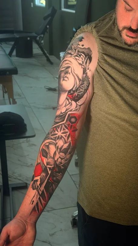 Tattoo of arm composition with a portrait, red geometric panels and angular patterns