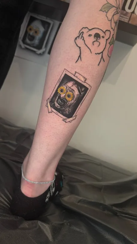 Small ghost figure and framed animal portrait tattoo on a forearm