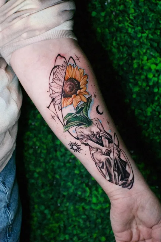 Orange sunflower, green leaves and seated figure with sun and moon symbols tattoo on an arm