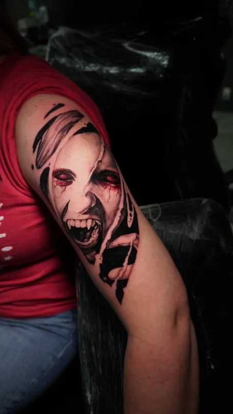 Black and grey vampire portrait with red eyes and mouth tattoo on an upper arm