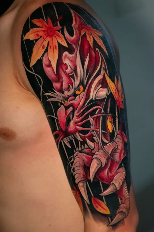 Red dragon tattoo with orange maple leaves and a black background on an upper arm
